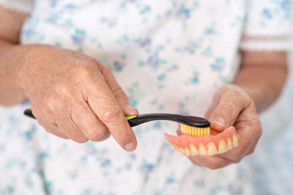 A woman brushing her dentures with a toothbrush.